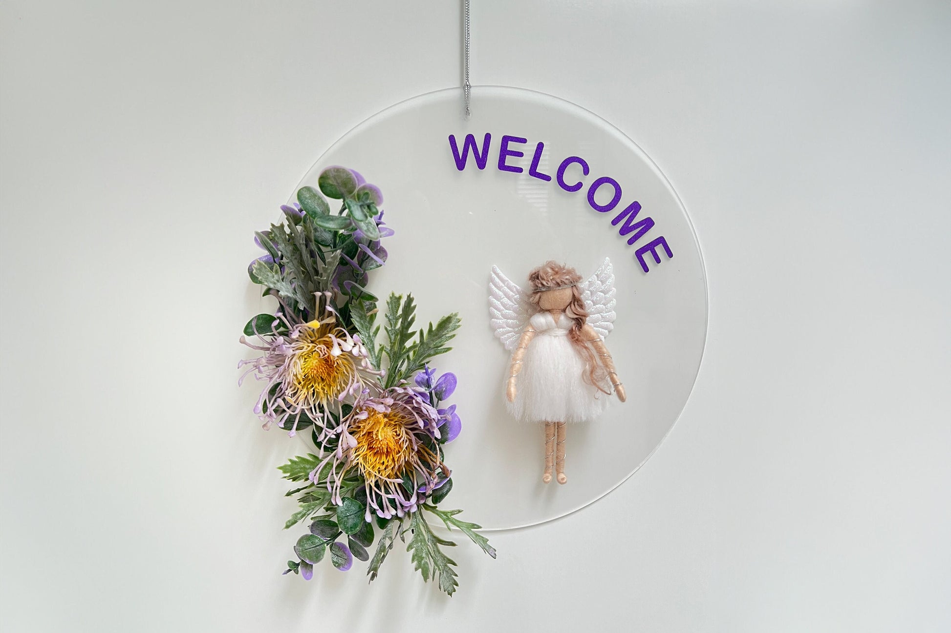 Decorative wall hanging with flowers, angel figurine, and 'WELCOME' text on a white background