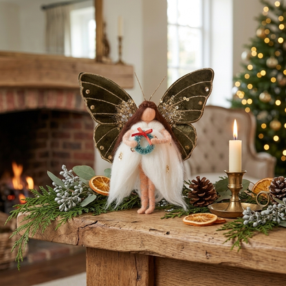 Handcrafted butterfly fairy ornament styled on a rustic holiday fireplace mantel alongside natural pine garland, dried citrus, and warm candlelight