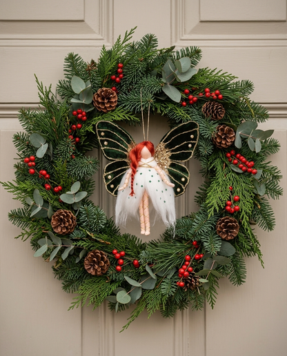 Emerald Butterfly Fairy hanging ornament (21 cm tall, 20 cm wide) styled centrally in the opening of a handcrafted festive evergreen wreath on an elegant door